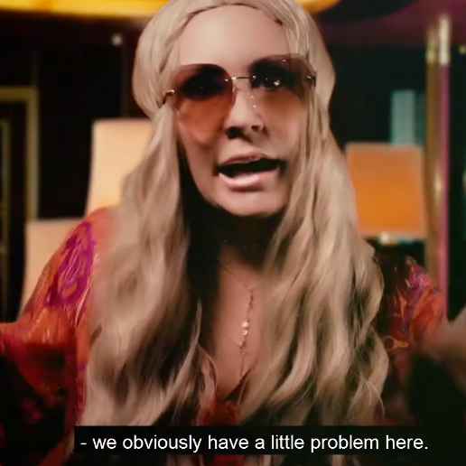 A woman with long blonde hair and sunglasses gestures with both hands in an indoor setting, with a subtitle at the bottom that reads, '- we obviously have a little problem here.'.